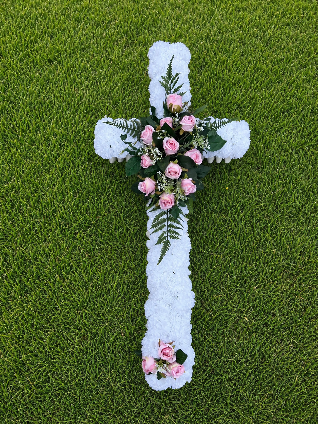 Handmade artificial funeral cross wreath in white and blue silk carnations on grass
